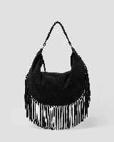 Cartera tipo hobo de gran tamaño en color negro, confeccionada en gamuza con diseño de flecos largos en los laterales y base. Presenta un asa superior trenzada con detalles artesanales y cierre superior para mayor seguridad.