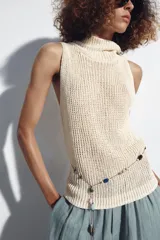 Top de punto color crudo, sin mangas, con cuello subido y diseño ajustado.
