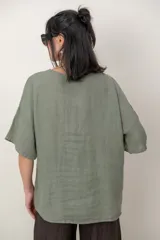 Blusa de lino color marrón oscuro, con escote redondo, mangas cortas amplias y detalle de alforzas verticales en el lateral derecho.