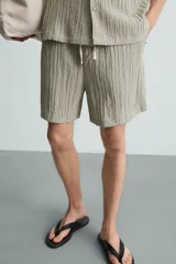 Bermuda negra de corte regular, confeccionada en tejido jacquard con efecto arrugado. Presenta cintura elástica ajustable con cordón blanco, bolsillos laterales y bolsillos traseros de vivo.