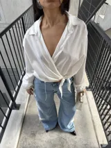 Camisa cruzada de color blanco, manga larga con puños amplios y lazo para atar en la cintura.
