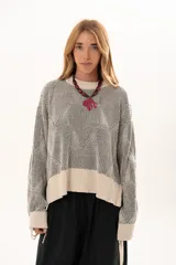 Buzo de tejido de punto con diseño geométrico en relieve, cuello redondo y mangas largas abullonadas con puños ajustables mediante lazos. Presenta un borde inferior en tejido acanalado de color crudo.