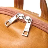 Mochila de cuero color suela con diseño compacto y redondeado. Cuenta con cierre superior, asa superior para llevar a mano y correas ajustables para usar en formato mochila. Presenta el logo de la marca grabado en la parte frontal.