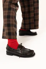 Zapato náutico de cuero color chocolate con horma cuadrada. Presenta detalles de pasamanería en cuero descarne que recorren el frente y los laterales, cordones frontales y suela plana con pequeño taco.