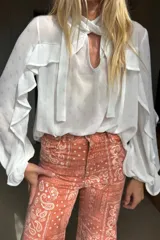 Blusa de gasa blanca con sutil estampado dorado, diseño con volados en las mangas y lazo en el cuello. Presenta una leve transparencia y caída fluida.