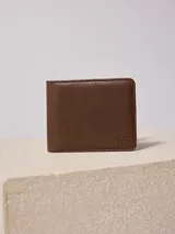 Billetera plegable Rusty Konroi de cuero sintético texturizado color marrón con logo de la marca grabado en la esquina inferior derecha. Interior forrado en poliéster con múltiples compartimentos para tarjetas y billetes.