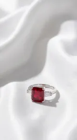 Anillo de plata con piedra central rectangular de color rojo intenso y piedras laterales tipo baguette.