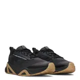 Championes de entrenamiento Under Armour modelo Charged Commit Tr 5, color gris oscuro con suela de goma en tono caramelo. Presentan diseño técnico con refuerzos laterales, logo de la marca en el lateral y lengüeta, y sistema de cordones para un ajuste seguro.