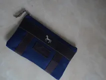 Sobre o cartuchera de lona fucsia con terminaciones y detalles de cuero marrón. Cuenta con cierre superior y aplique metálico de caballo en la parte frontal, además de una etiqueta de cuero con la marca grabada.