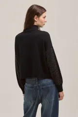 Sweater de punto negro con cuello alto y diseño de puntos brillantes en contraste. Presenta mangas largas con puños ajustados y un corte recto a la cintura.