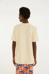 Remera beige de algodón con diseño estampado frontal que incluye la palabra "Samba" y cuatro loros de colores.