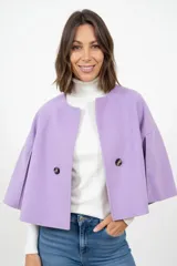 Capa corta de paño en color lila, con cuello redondo, cierre frontal de dos botones y mangas amplias tipo capa con pliegues laterales.