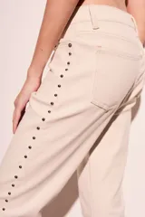 Pantalón de jean color crudo, corte flare, tiro medio y detalle de tachas plateadas en los laterales.