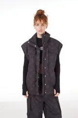 Chaleco negro con estampado de logos, cuello alto, cierre frontal con cremallera y broches a presión ocultos, bolsillos delanteros y cintura ajustable con cordón elástico. Interior de tafeta relleno de guata.