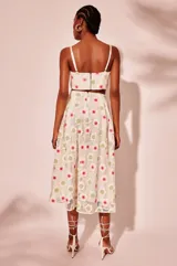 Vestido midi blanco con bordados de flores en tonos fucsia y verde, tirantes finos ajustables, escote recto y aberturas laterales en la cintura.
