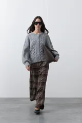 Cardigan gris de tejido de punto con diseño de trenzas, cuello redondo, cierre frontal con botones y mangas largas con puños acanalados.