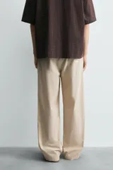Pantalón relaxed fit color beige con rayas verticales finas, confeccionado en tejido de algodón. Cuenta con cintura elástica ajustable con cordón, bolsillos frontales y bolsillos traseros de plastrón.