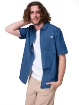 Camisa de manga corta en denim ligero de color azul, con cierre frontal de botones, cuello camisero y un bolsillo en el pecho con solapa y botón.