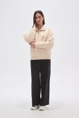 Buzo de algodón color tostado, con cuello polo y cierre frontal parcial con botones. Presenta un detalle de forro de corderito sintético blanco en el cuello y mangas largas con diseño holgado.