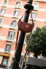 Cartera pequeña de diseño semicircular con textura tipo crocco en color bordó. Presenta herrajes metálicos en bronce y una correa ajustable y versátil que permite diferentes formas de uso.