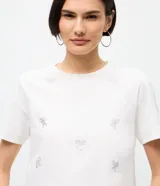 Remera de algodón de corte clásico con cuello redondo y manga corta. Presenta un diseño estampado con pequeños lazos formados por aplicaciones de hotfix brillantes distribuidos por toda la prenda.