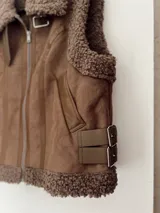 Chaleco marrón con forro de corderito, cierre frontal con cremallera y bolsillos laterales.