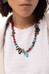 Collar corto de diseño artesanal compuesto por una variedad de cuentas de piedras naturales, cristales checos y acrílicos en tonos multicolor, incluyendo rojo, azul, turquesa y gris. Presenta un dije central en forma de gota color turquesa y cierre con cadena de acero quirúrgico ajustable.