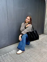 Cartera tipo tote bag de gamuza negra, con detalles de costuras decorativas en forma de X y tiras de cuero entrelazadas en el frente. Cuenta con doble asa de hombro y cierre superior.