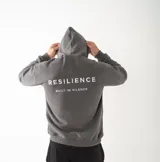Canguro unisex de corte oversize confeccionado en felpa premium de alto gramaje. Presenta capucha, mangas largas con puños acanalados y diseño con bordado en la espalda que incluye la frase 'RESILIENCE BUILT IN SILENCE'.