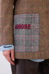 Blazer de corte sastrero confeccionado en paño con estampado de cuadros escoceses. Presenta parches decorativos en las mangas y espalda, bordados en el bolsillo y manga, y cierre frontal con botones.