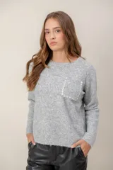 Sweater de punto gris con cuello redondo, manga larga y bolsillo frontal decorado con botones brillantes.