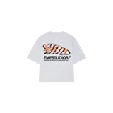 Remera oversize gris melange de manga corta, con estampa frontal de diseño abstracto en tonos negros y naranjas, acompañada por el texto "Emestudios" y la leyenda "Inspired by metropolitan lifestyle".