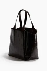 Bolso tote de mano, color marrón oscuro o negro, con textura de cocodrilo en charol. Presenta dos asas superiores fijas y un diseño amplio y estructurado.