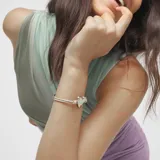 Pulsera ajustable de cordón de cuero color beige/camel con un dije central de corazón dorado de aspecto martillado. Presenta un cierre de bola dorada ajustable.