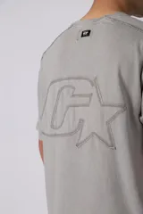 Remera de algodón gris con efecto acid wash, corte regular, mangas cortas y cuello redondo. Cuenta con un pequeño bordado tono sobre tono en el pecho y una etiqueta lateral distintiva de la marca en el ruedo.
