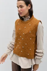 Chaleco de punto color celeste, con diseño de trenzas y pequeñas flores bordadas a mano en color marrón oscuro. Presenta cuello redondo y terminaciones acanaladas.