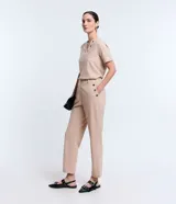 Pantalón slim color beige, confeccionado en crepé, con cierre delantero en la cintura y detalles de ojales en los bolsillos.