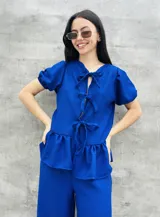 Blusa estampada con hojas verdes y blancas, con escote en V y mangas cortas abullonadas. Presenta volados en el ruedo y detalle de lazos en el frente.