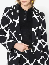 Blazer negro con estampado geométrico blanco, cuello con solapa, acceso con broche y bolsillos plaque.