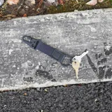 Llavero negro con cinta de tela, aplique de cuero con logo y mosquetón metálico.