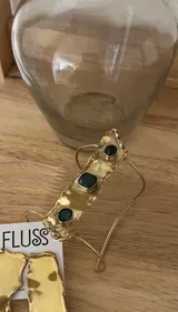 Brazalete rígido dorado con tres piedras verdes incrustadas.