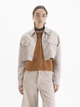 Chaqueta corta estilo jeanero, color beige claro, confeccionada en algodón. Presenta botones metálicos y remaches decorativos en el cuello.