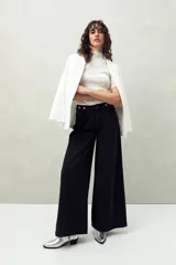 Pantalón de jean negro de corte ultra wide, tiro medio y detalles metálicos en la cintura.