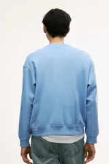 Buzo azul claro de tejido de mezcla de algodón, con interior cepillado suave, cuello redondo ribeteado, hombros caídos y remate acanalado ancho en puños y bajo. Corte holgado.