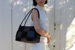 Cartera de hombro con diseño de patchwork que alterna paneles de cuero liso y gamuza en color marrón oscuro. Presenta doble asa trenzada y estructura rectangular.