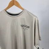 Remera color beige de algodón con estampa en la espalda con el texto "Cafe del Mar Ibiza" y una frase en inglés. Corte clásico y cuello redondo.