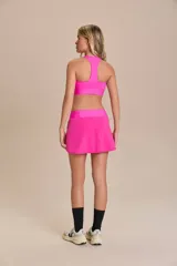 Pollera deportiva color rosa fucsia, con estampado en relieve de texto. Es de corte corto con ruedo redondeado y cuenta con shorts internos.