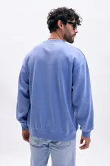 Buzo deportivo de cuello redondo, color azul medio con efecto lavado, de corte holgado y manga larga.
