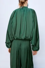 Pantalón de tiro medio confeccionado en tejido satinado verde, con diseño bombacho y bajos acabados en puño elástico. Cuenta con cierre lateral con cremallera oculta en costura.