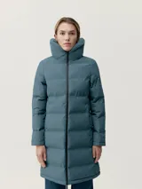 Campera larga tipo puffer de acabado mate, con cuello alto envolvente, cierre frontal con cremallera y bandas acolchadas termoselladas. Cuenta con bolsillos laterales con cremallera oculta y relleno vegano.
